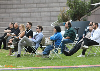Festival attendees seated outdoors . One of the audience members is wearing headphones for audio description services.