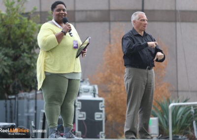 MC Nikki Bailey is on stage, smiling looking toward the camera with the mic in her hand. To her right is an ASL interpreter.