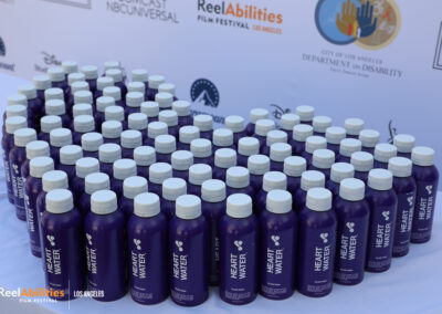 Heart water bottles stacked on a table in the shape of a heart. Step and repeat are in the background with the department of disability logo and ReelAbilities film festival logo among other festival sponsors and supporters.