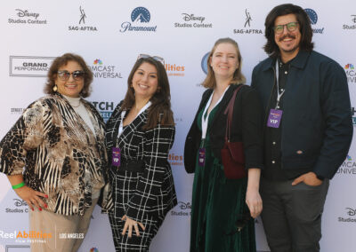 A group of festival attendees posing in front of the step and repeat. They are all smiling and facing the camera wearing VIP badges.