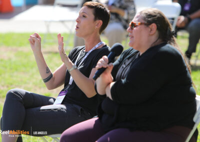 An audience member holding the mic addressing the panelist. An ASL translator sitting next to her on her right side signing with one of the panelists.