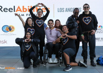 Members from Straight Up Abilities and Danny Gomez. Danny is stagged in the middle with his wheelchair,the dancers are gathered around him posing in various dance moves and smiling, facing the camera.