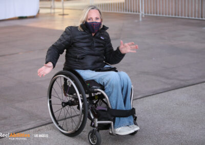 Photo of Candace Cable sitting in her own wheelchair wearing a facemask facing the camera.