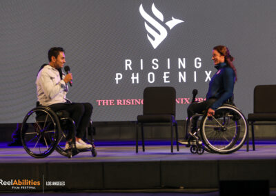 Photo of Danny Gomez and Tatyana McFadden on the main stage. Danny is holding the mic addressing Tatyana.