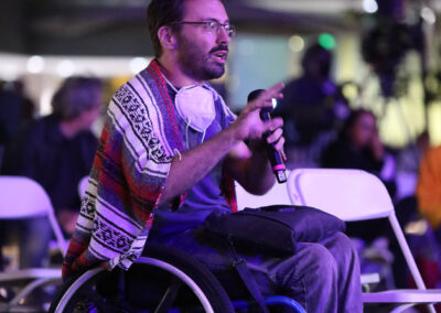Festival attendees during a panel discussion. Attendee David Radcliff is sitting in a wheelchair, holding a mic and asking a question.